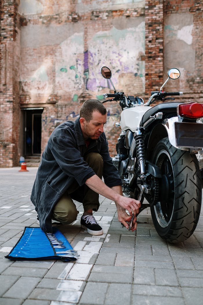 Man using a wrench to repair a motorcycle in an urban environment with brick wall backdrop.