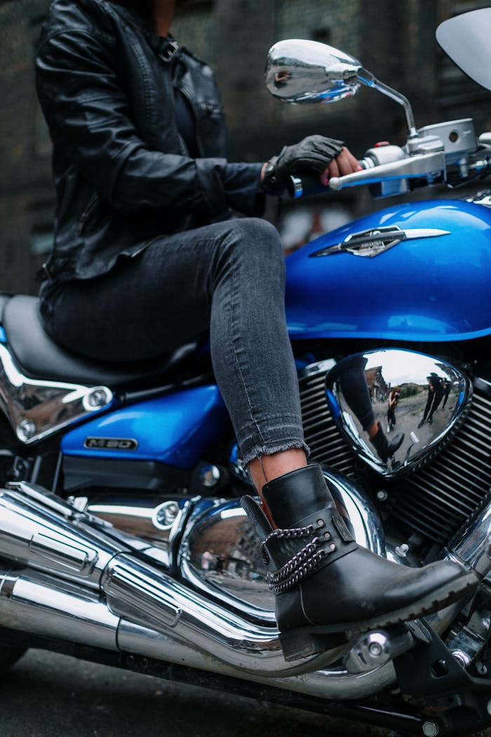 Close-up of a woman sitting on a blue motorcycle wearing black leather gear. Urban vibe.