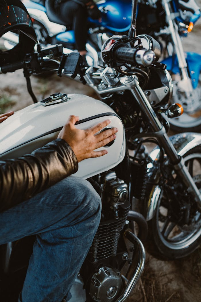 A biker in a leather jacket touches the gas tank of a motorcycle.
